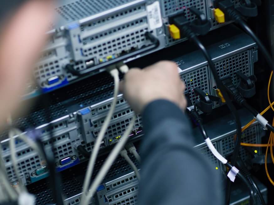 Someone inserting cables into the back of servers or other equipment.